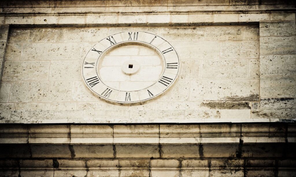 Ancient wall clock with Roman numerals carved into a stone wall, missing hands.