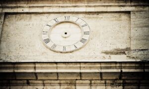 Ancient wall clock with Roman numerals carved into a stone wall, missing hands.