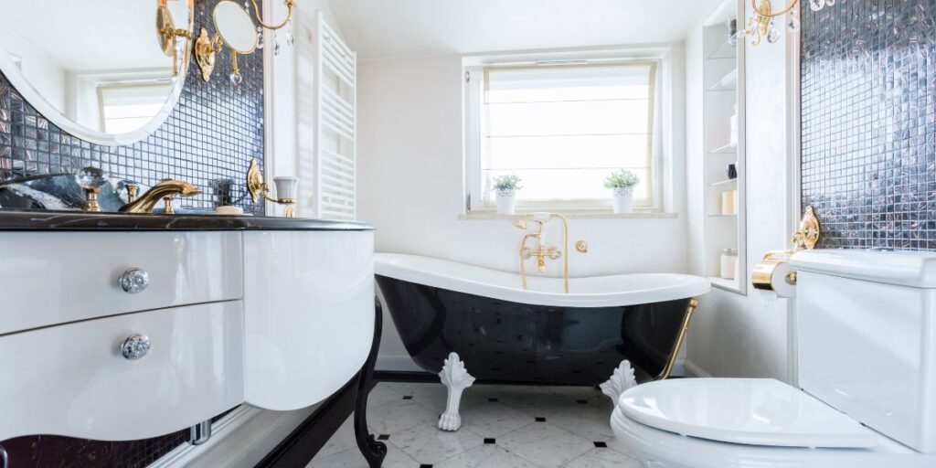 Timeless design Elegant bathroom with a black clawfoot tub, marble countertops, gold fixtures, and a decorative mirror against a tiled wall.