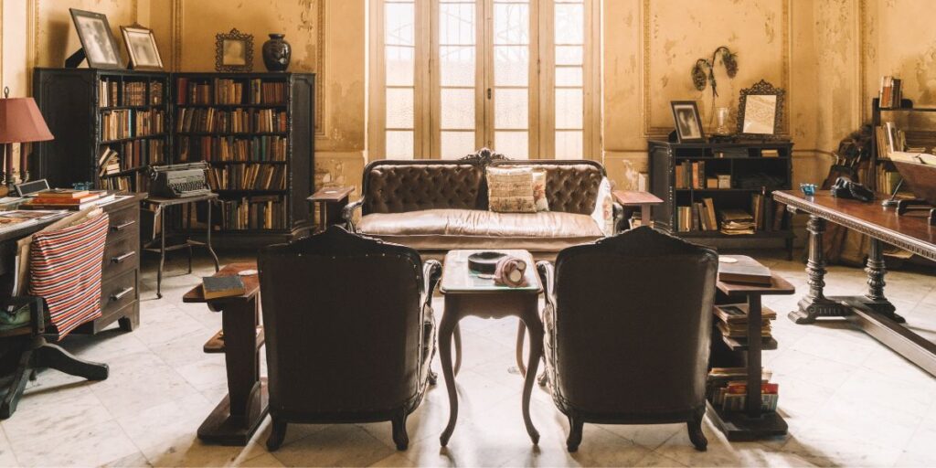 Vintage study room with leather chairs, a tufted sofa, wooden bookshelves filled with books, and a typewriter on a side table.
