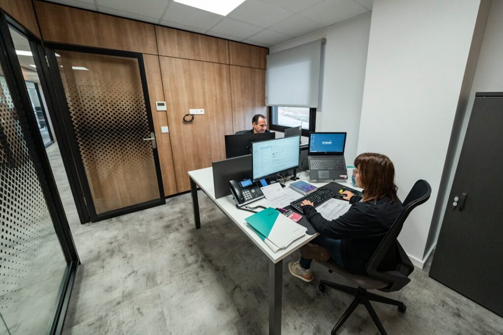 Professionally dressed person looks concerned and thoughtful while talking on the phone in a modern, bright office setting...
