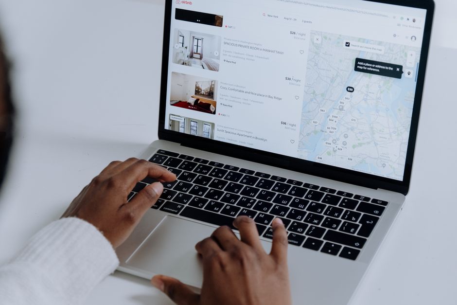 An overhead view of a person's hands on a laptop keyboard, browsing a website with photos of modern homes for sale.